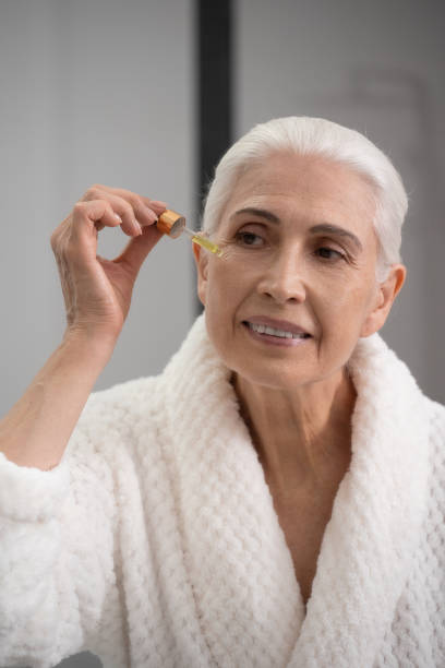 femme âgée attrayante avec compte-gouttes appliquant du sérum sur le visage - model70 photos et images de collection