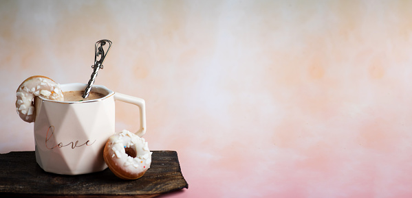 White tea cup and two white donuts with chocolate sprinkles on a romantic background