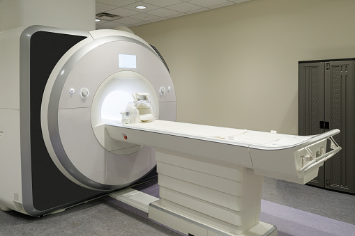 An fMRI machine.  Functional magnetic resonance imaging (fMRI) measures the small changes in blood flow that occur with brain activity. It may be used to examine the brain's functional anatomy, (determine which parts of the brain are handling critical functions), evaluate the effects of stroke or other disease, or to guide brain treatment. fMRI may detect abnormalities within the brain that cannot be found with other imaging techniques.  The machine is pictured without any people.  A set of plastic lockers can be seen on the right of the frame.
