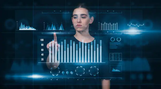 Photo of A scientist, businesswoman looking at the charts to analyze the data. She is looking at the digital screen, a hologram. Virtual Reality has taken place in the business world. This is a futuristic photo. High-Tech, Augmented Reality, Virtual Reality Concep