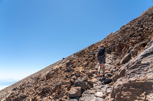 One teenager boy hiking on footpath up the top of volcano Pico de Teide against clear blue sky.