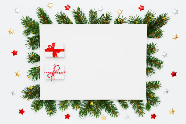 istock Christmas, New Year holiday layout with copy space for text. Blank white paper with two small Christmas gifts in frame of natural fir tree branches, decorations, confetti, stars on white flat lay background 1359556315
