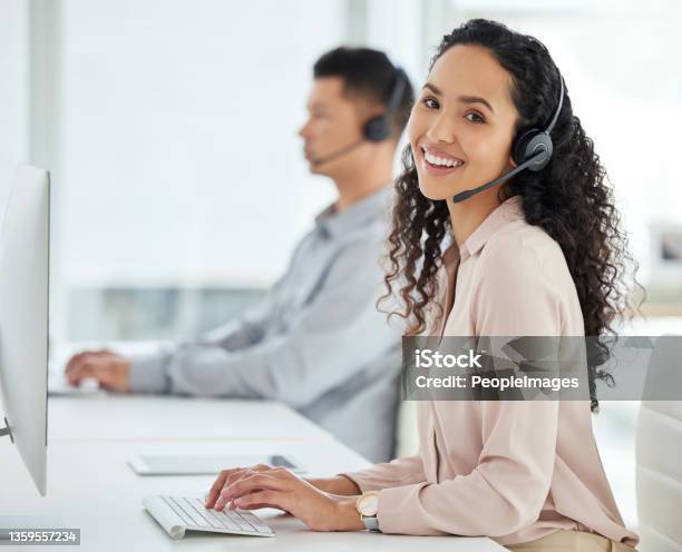 Portrait Of A Young Call Centre Agent Working On A Computer In An Office With Her Colleague In The Background Stock Photo - Download Image Now