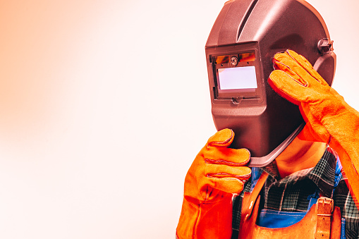 Metallurgist in a protective suit, gloves, taking off his welding mask, Close-up, Fire colors