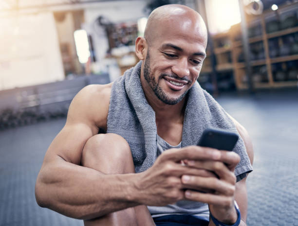 istock Shot of a muscular young man using a cellphone while taking a break from exercising in a gym 1359559979