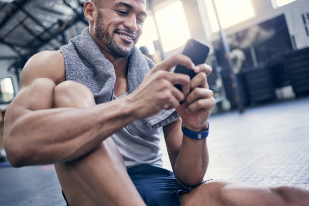 istock Shot of a muscular young man using a cellphone while taking a break from exercising in a gym 1359559983