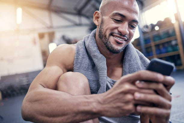 istock Shot of a muscular young man using a cellphone while taking a break from exercising in a gym 1359559994