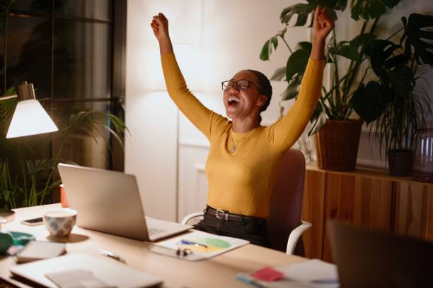 istock Attractive young businesswoman cheering while working on a laptop at night 1359563436