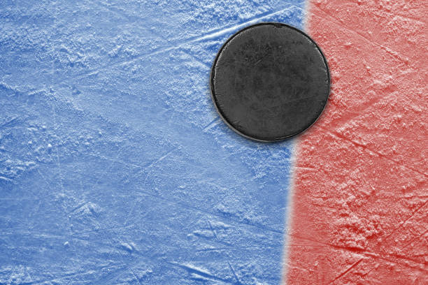 istock Hockey puck on blue ice with red stripe 1359563439