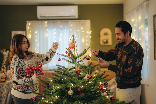 Couple decorating a Christmas tree. Young man and woman decorate the Christmas tree in living room at home.