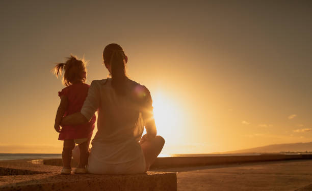 Mother with her two year old daughter watching sunset at the beach together.