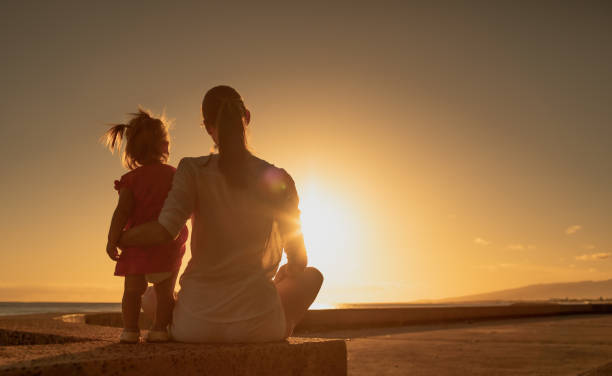 Mother and daughter watching beautiful sunset at the beach stock photo