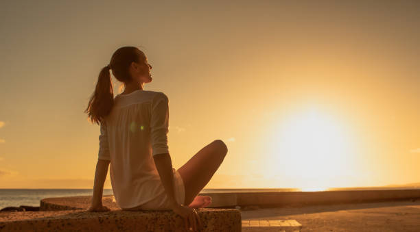 istock Woman sitting on the beach at sunset. 1359566188