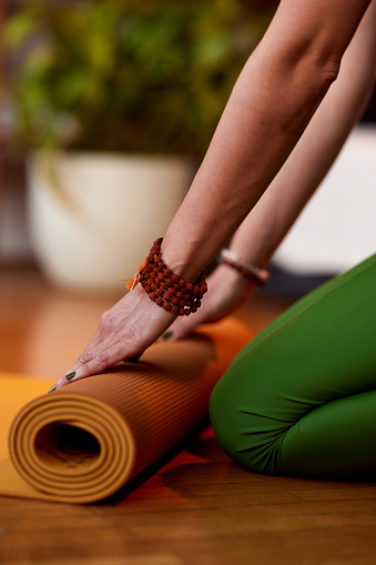 Close up of yogi woman's hands rolling up a yoga mat at home. Hands rolling yoga mat.