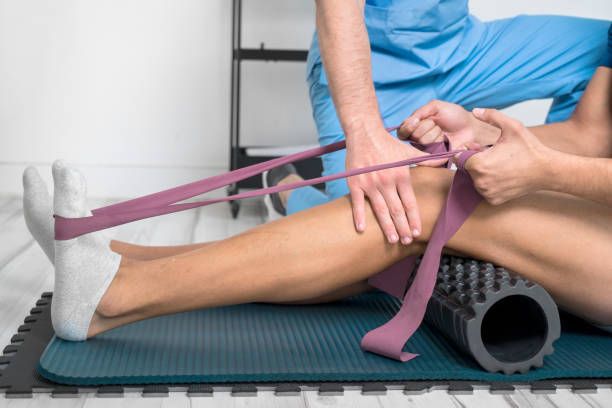 joven usando cinturón de yoga mientras hace ejercicio en la colchoneta de fitness en la clínica de rehabilitación. foto de alta calidad - biomecánica fotografías e imágenes de stock