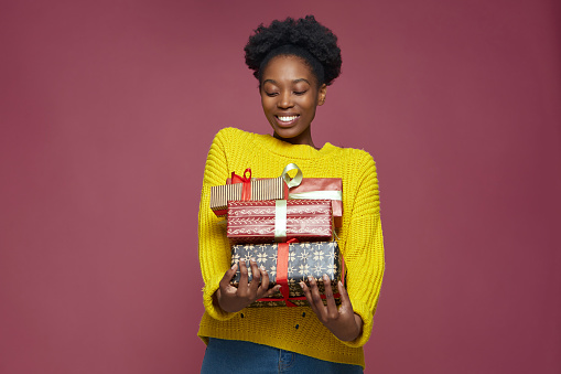 Happy young african american woman holding gift boxes smiling, enjoying many presents, celebrating xmas or birthday holiday. High quality photo