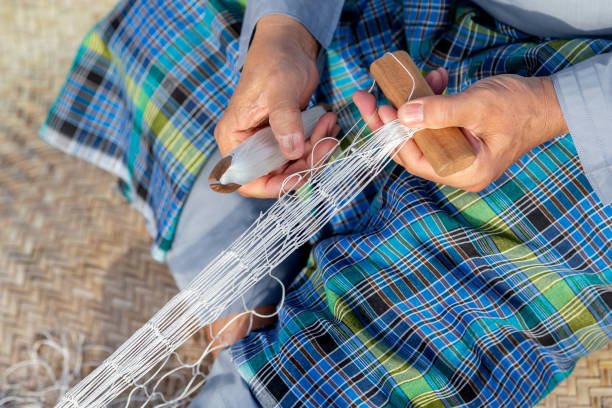 Old man is knitting traditional fishing net, hands in frame. High quality photo.