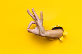The woman's hand shows with a gesture that everything is fine (ok). Torn hole in yellow paper. The concept of a positive attitude to life, joy and harmony. Zero symbol. Copy space.