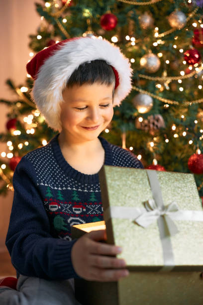 istock A cute boy opens a gift near the New Year tree. Christmas miracle 1359583490