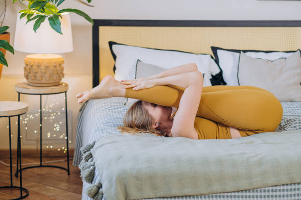 istock Blonde-haired woman does yoga stretching lying on bed 1359584950