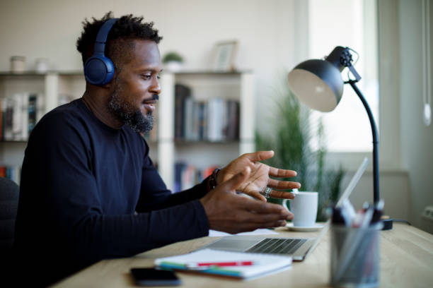 istock Smiling man with headphones having video call on laptop computer in his home office 1359589682