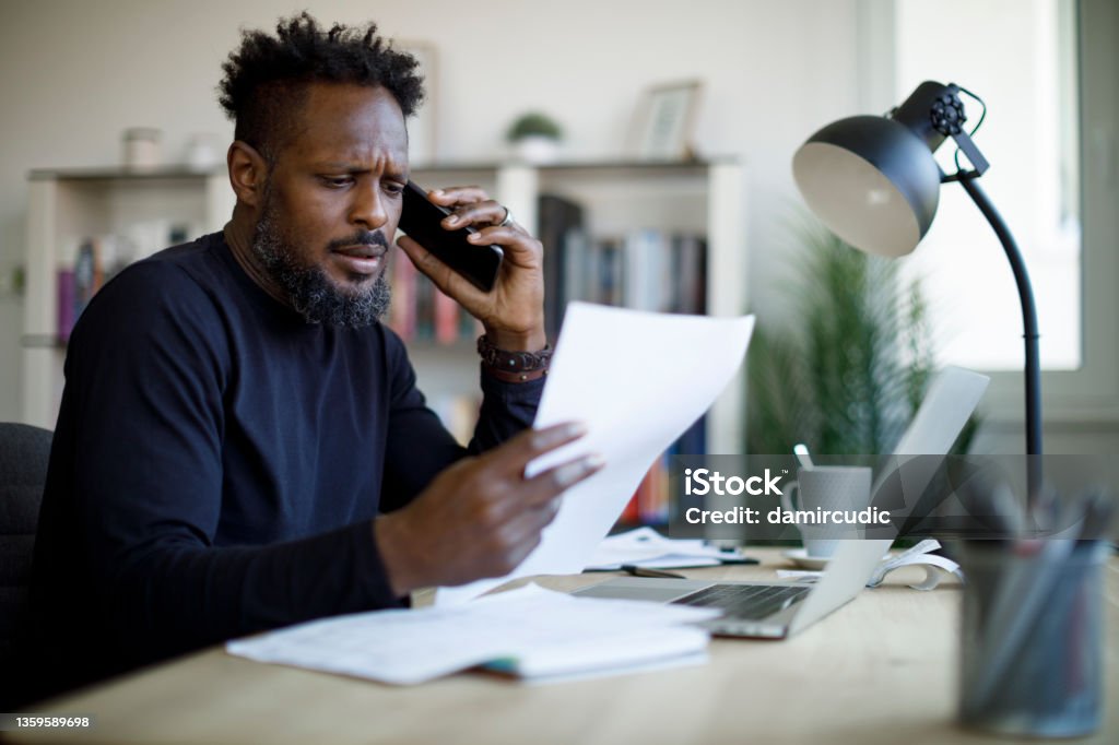 Worried man talking on the phone while working from home Using Phone Stock Photo