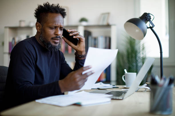 worried man talking on the phone while working from home - frustration computer confusion businessman imagens e fotografias de stock