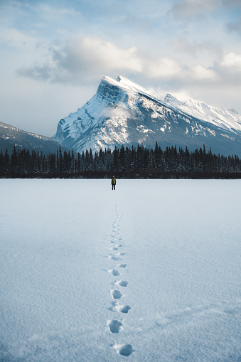 A man walks on a frozen snow covered lake towards a snow capped mountain in Banff, Alberta