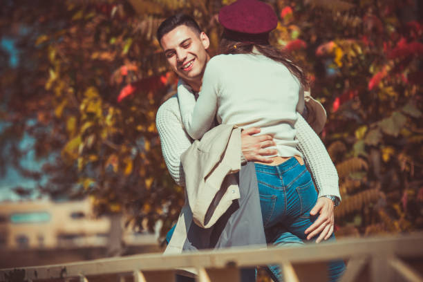 парень держит свою девушку в руках в парке - couple autumn embracing bridge стоковые фото и изображения