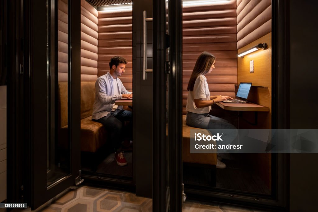Casual business people working in an isolated booth at the office Casual Latin American business people working in an isolated booth at the office Coworking Stock Photo