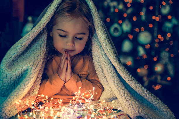 Kid Making Magic Wish for Winter Holidays. Baby Near the Christmas Tree at Home. Under the Plaid Praying. Waiting for Santa at Night.