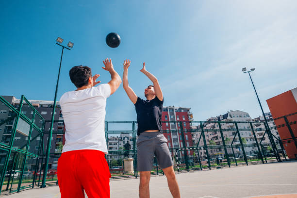 deux athlètes jouant un match de basket-ball de rue sur un terrain de basket-ball urbain (se poussant, se tirant l’un l’autre et tirant pour trois). - building block photos et images de collection