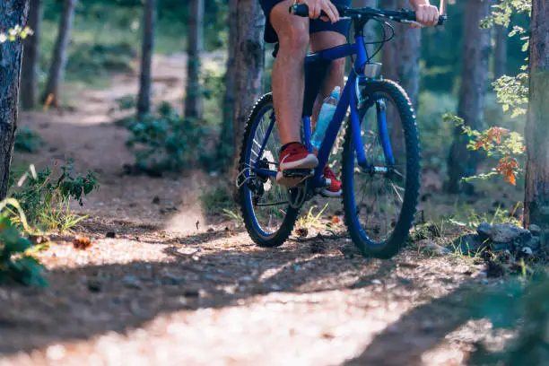 Photo of Fit cyclist riding his bike downhill through a forest ( woods ) while wearing a red shirt and red shoes.