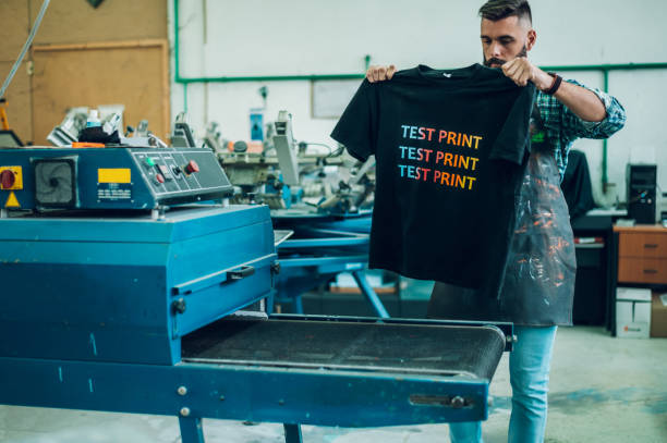 männlicher arbeiter mit einem trockenschrank für t-shirt in einer werkstatt - ausdrucken stock-fotos und bilder