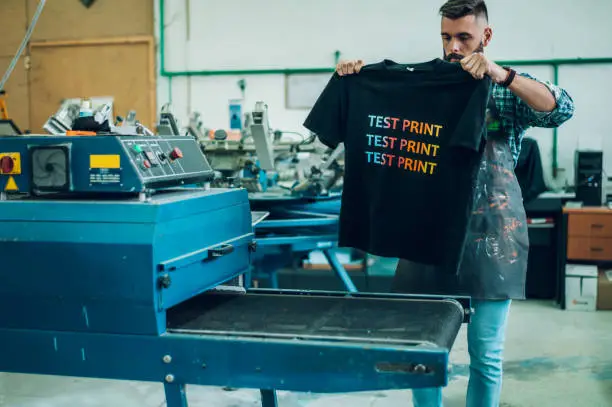 Photo of Male worker using a drying oven for t-shirt in a workshop