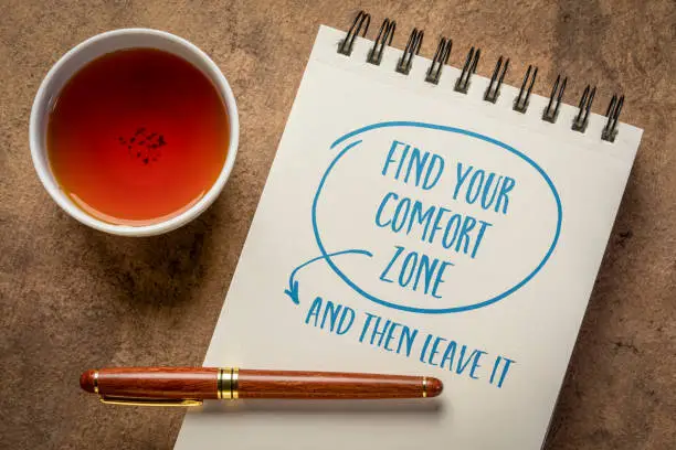 Find your comfort zone and then leave it - inspirational handwriting in a spiral notebook with a cup of tea, challenge and personal development concept