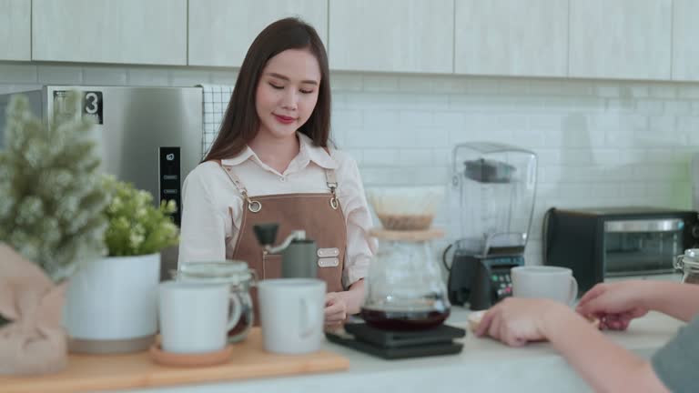 Smiling barista serving a coffee to her customer ,Asian woman paying qr code for coffee using smartphone in coffee shop