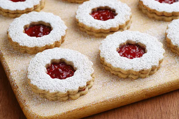 Raspberry Linzer Torte cookies on a cutting board with powdered sugar sprinkled on top.