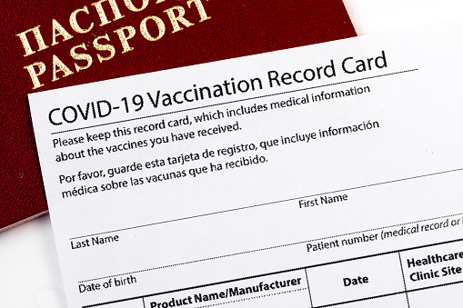 Coronavirus vaccination record card, biometric passport and blue medical mask on light gray desk. Concept of defeating Covid-19. Vaccination as prerequisite for travel