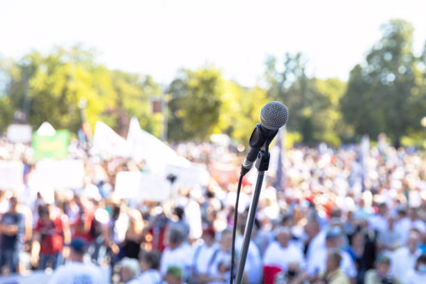 Focus on microphone, blurred group of people at mass protest or public demonstration in the background