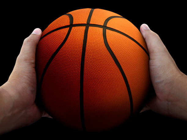 istock Basketball player holding a ball against black background 1359658389