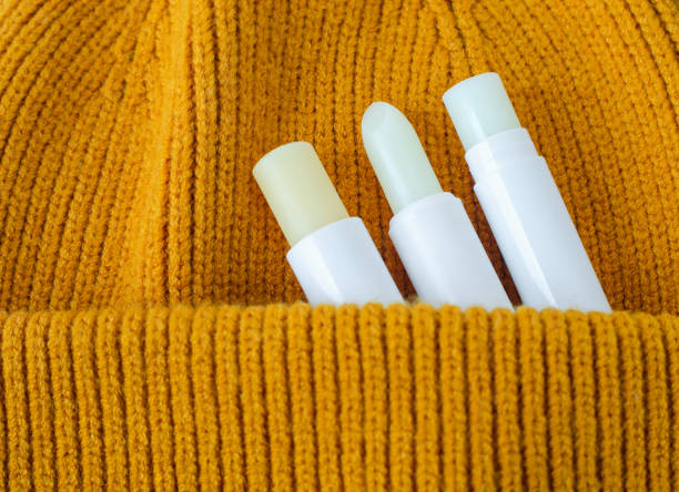 Three lip balms on an orange knitted background. Winter lip care sticks with beeswax, honey, panthenol and shea butter. Copy space. Three lip balms on an orange knitted background. Winter lip care sticks with beeswax, honey, panthenol and shea butter. Copy space. vitamin b 3 stock pictures, royalty-free photos & images