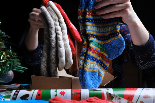 Unrecognizable woman is packing handmade socks and mittens and wrapping Christmas gifts