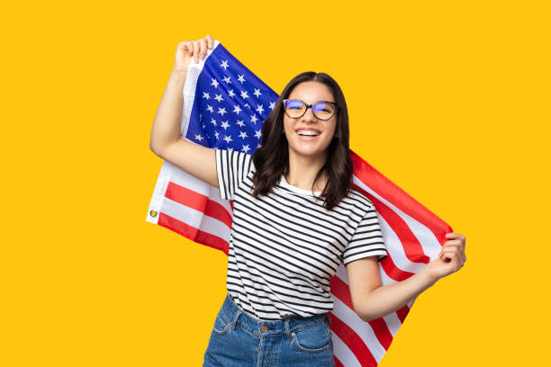 молодая жизнерадостная многонациональная женщина держит американский флаг на желтом фоне - day 4 стоковые фото и изображения