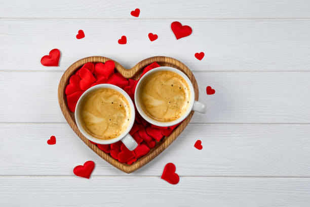 due tazze di caffè su un vassoio a forma di cuore e cuori rossi su uno sfondo di legno bianco. biglietto di auguri per san valentino - morning coffee coffee cup two objects foto e immagini stock