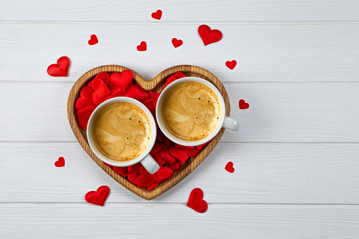 Two cups of coffee on a tray in the shape of a heart and red hearts on a white wooden background. Festive card for Valentines Day. High quality photo