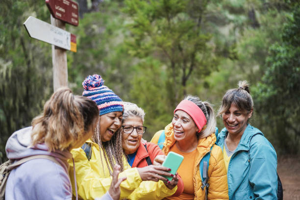 istock Multiracial women having fun using mobile phone for web map while trekking into the wood - Focus on caucasian senior face 1359667254