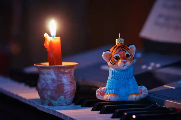 Photo of 2022 tiger. New Year's composition on the keys of the synthesizer with candles. Notes on the music stand. Selective focus.