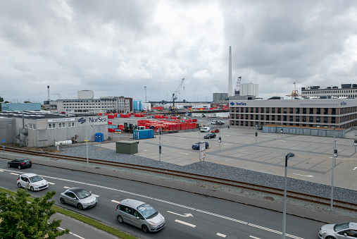 near the streets Toldbodvej and Østre Havnevej. In the foreground there are cars on the street, a train track runs parallel to the street, behind it there are buildings, harbor cranes and a large chimney. 07/31/2021 - Toldbodvej, 6700 Esbjerg, Jutland, Denmark