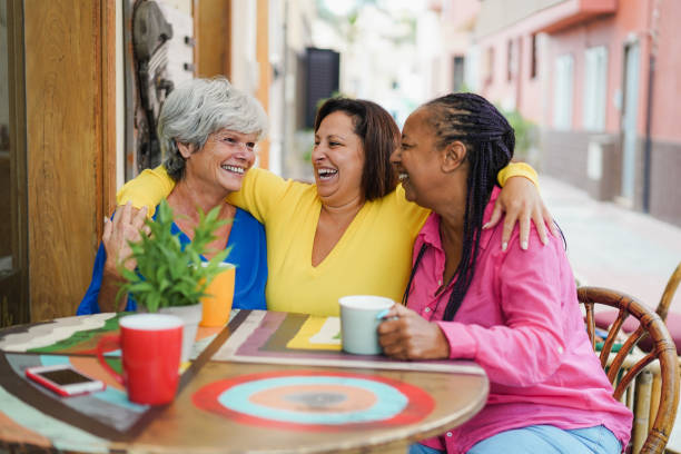 istock Multiracial senior friends having fun hugging at bar outdoor while drinking coffee together - Focus on right woman face 1359669718